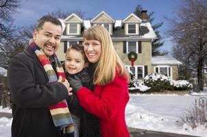 familia de raza mixta frente a la casa en la nieve foto