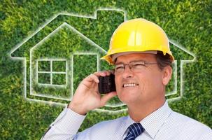 contratista en casco en el teléfono celular sobre el icono de la casa y la hierba foto
