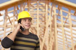 Hispanic Male Contractor on Phone in Front of House Framing photo