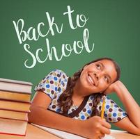 Cute Hispanic Girl Studying and Looking Up to Back To School Written on Chalk Board photo