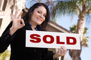 Attractive Hispanic Woman Holding Sold Sign In Front of House photo