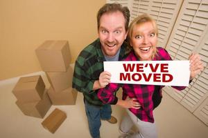 Goofy Couple Holding We've Moved Sign Surrounded by Boxes photo