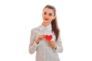 hermosa joven morena con corazón rojo en las manos posando aislada sobre fondo blanco. concepto del día de san valentín. concepto de amor foto