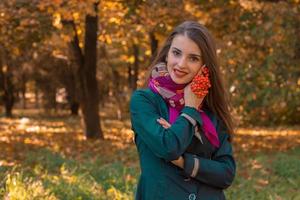 cute girl stands in autumn Park with a sprig of Rowan in her hand photo