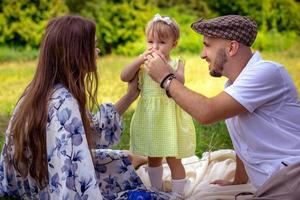 Parents with daughter relaxing at the picnic time outdoors photo