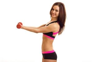 cute athletic girl stands sideways in front of the camera, smiles and holds out her hands forward with dumbbells photo