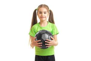 linda niña con camisa verde sosteniendo una pelota de fútbol en las manos foto