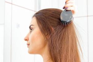 Portrait of a young girl who stands sideways in the bathroom and combs her hair photo