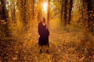 Attractive young blonde girl in black coat in autumn forest photo