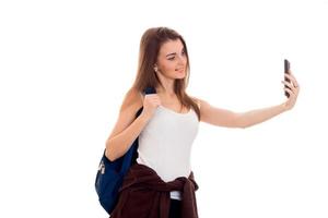 young smiling girl holding on his shoulder backpack and shoots himself on the phone photo