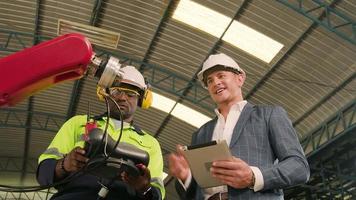 An African American engineer demonstrates smart robotic arm control to customer in mechanical manufacturing factory, intelligent automatic machines in industrial business, and futuristic technology. video