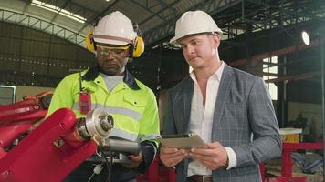 un ingénieur afro-américain démontre un contrôle intelligent du bras robotique au client dans une usine de fabrication mécanique, des machines automatiques intelligentes dans le secteur industriel et une technologie futuriste. video