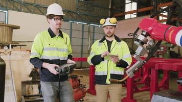 Due caucasico maschio produzione ingegneri test e controllo un' robotica braccio nel meccanico produzione fabbrica, intelligente automatico macchine nel industriale attività commerciale, e futuristico tecnologia innovazione. video