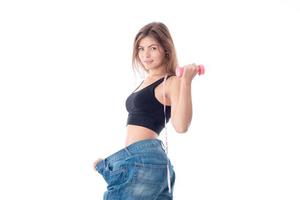 Slim young girl in big jeans holding a dumbbell in your hand isolated on white background photo