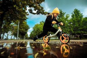 Cutie little girl rides through the puddles on bicycle at the park photo