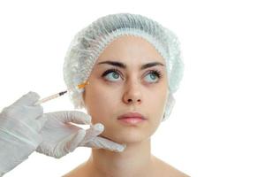 Portrait of a pretty young girl in a special hat on your head which makes injection syringe on face close-up photo