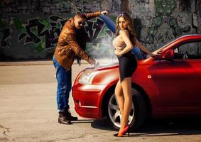 Fashion male model reparing car for voluptuous blonde young woman photo