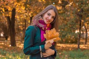 young girl stands smiling in the Park and keeps the leaves from the trees photo