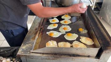 A man fries a lot of eggs on the stove making fried eggs in the kitchen in a cafe or restaurant