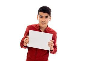 Un joven moreno con estilo posando con un cartel vacío en las manos y sonriendo a la cámara aislado de fondo blanco foto