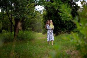 pretty young woman walks carrying little baby girl at the garden photo