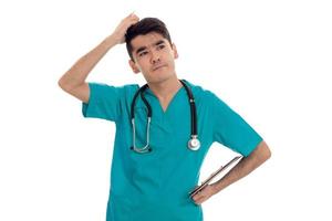 thoughtful young male doctor in uniform with stathoscope posing isolated on white background photo