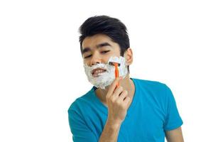 young guy with foam on his face shaves his beard machine close-up photo