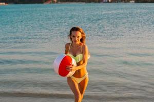 adorable dama delgada en traje de baño con pelota de playa en el mar foto