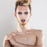 atractivo modelo masculino mirando a la cámara con maquillaje y barba multicolor foto