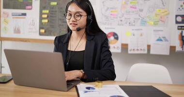 Side view of Happy female glasses wears headset video calling on laptop. Businesswoman webinar speaker streaming live web training. Call center agent, service support manager speaking to customer.