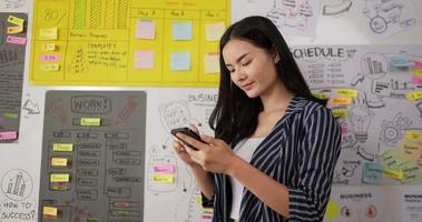 Portrait of attractive businesswoman texting message on smartphone at workplace. Smiling lady using cellphone at office room. Cheerful woman chatting online on mobile phone. video