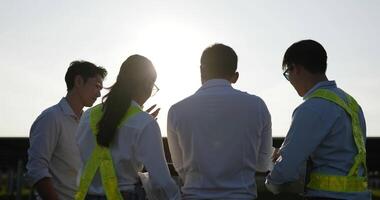 Backlit shot, Rear view Group of Asian engineering team use laptop during planning operation and photovoltaic solar panel in station, Young Inspector Engineer men and female planning operation video