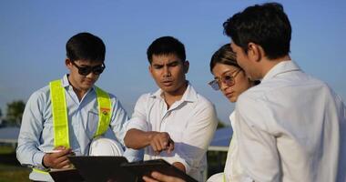 tiro de perto, grupo de equipe de engenharia asiática usa laptop durante a operação de planejamento e painel solar fotovoltaico na estação, homens jovens engenheiros inspetores e operação de planejamento de colega video