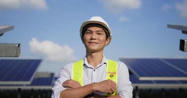 Handheld shot, Close up portrait of young engineer man in protective helmet. standing crossed arms, looking at camera and smiles in solar farm video