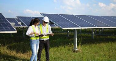 Asian Young Inspector Engineer man and female colleague wearing helmet standing and checking operation in solar farm video