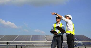 tir à la main, jeune ingénieur asiatique et collègue en casque de protection blanc, ils sont debout en train de parler et de vérifier le fonctionnement dans une ferme solaire
