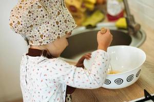linda niñita homecook hace panqueques en la cocina blanca. foto
