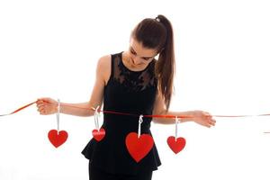a young girl in a black dress lowered her head down and holding a Red Ribbon with hearts photo
