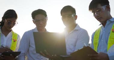 tir rétroéclairé, un groupe d'équipes d'ingénieurs asiatiques utilise un ordinateur portable et une tablette pendant l'opération de planification et un panneau solaire photovoltaïque dans la station, de jeunes inspecteurs ingénieurs hommes et femmes pour l'opération de planification