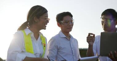 tir rétroéclairé, un groupe d'équipes d'ingénieurs asiatiques utilise un ordinateur portable et une tablette pendant l'opération de planification et un panneau solaire photovoltaïque dans la station, de jeunes inspecteurs ingénieurs hommes et femmes pour l'opération de planification video