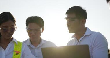 hintergrundbeleuchtete aufnahme, gruppe des asiatischen ingenieurteams verwendet laptop und tablet während des planungsvorgangs und photovoltaik-solarpanel in der station, junge inspektoringenieure und weibliche planungsvorgänge video