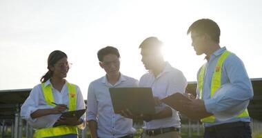 toma retroiluminada, un grupo de ingenieros asiáticos usa una computadora portátil y una tableta durante la operación de planificación y el panel solar fotovoltaico en la estación, los jóvenes ingenieros inspectores y las operaciones de planificación femenina video
