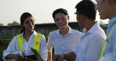 tir rétroéclairé, un groupe d'équipes d'ingénieurs asiatiques utilise un ordinateur portable et une tablette pendant l'opération de planification et un panneau solaire photovoltaïque dans la station, de jeunes inspecteurs ingénieurs hommes et femmes pour l'opération de planification video