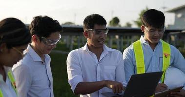 tir rétroéclairé, un groupe d'équipes d'ingénieurs asiatiques utilise un ordinateur portable et une tablette pendant l'opération de planification et un panneau solaire photovoltaïque dans la station, de jeunes inspecteurs ingénieurs hommes et femmes pour l'opération de planification