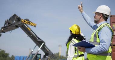 Kaukasisch ingenieur Mens en vrouw voorman arbeider vervelend helm en veiligheid hesje controle bezig met laden een Verzending container, gebruik hand- signaal terwijl hijs- containers doos van lading, logistiek concept video