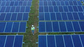 vista aérea do drone sobre jovem inspetor engenheiro asiático usando capacete de proteção segura papelada caminhando entre a fileira do painel solar enquanto verifica a operação na estação solar à noite video