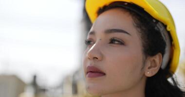 ritratto vicino su viso di bellissimo ingegnere donna Riccio capelli indossare casco e veste In piedi e girare viso per Sorridi e Guarda a il telecamera mentre Lavorando nel contenitore terminale porta video