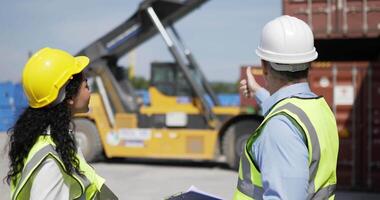 Caucasian Engineer man and female foreman worker wearing helmet and safety vest control loading a shipping Container site work, use sign hand while lifting containers box from cargo, Logistic concept video