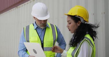 toma de mano, gerente de negocios caucásico de mediana edad y linda ingeniera están revisando el contenedor de transporte y usan una computadora portátil en la terminal del puerto de almacenamiento video