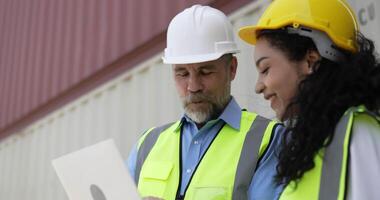 toma de mano, gerente de negocios caucásico de mediana edad y linda ingeniera están revisando el contenedor de transporte y usan una computadora portátil en la terminal del puerto de almacenamiento video